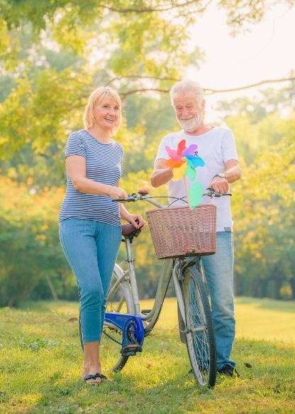 Two elderly people walking on grass with a bicycle