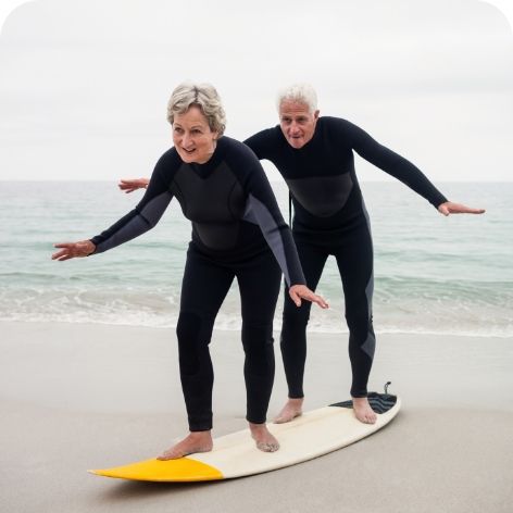 Two elderly people standing on a wake board on a beach