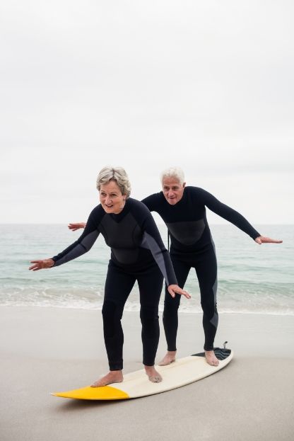 Two elderly people standing on a wake board on a beach