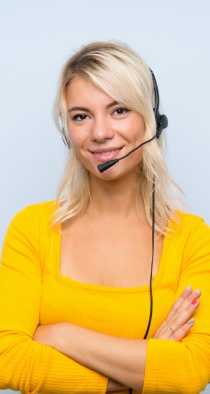 A portrait view of a person with a yellow top crossing their arms while wearing a headset